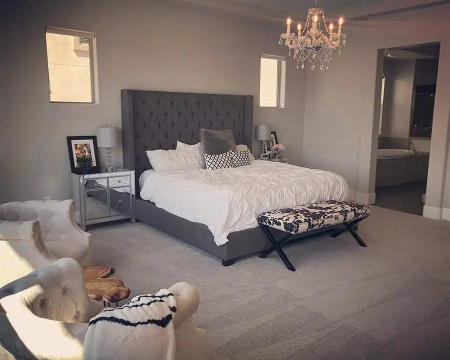 Elegant grey and white bedroom with a tufted headboard, crystal chandelier, and cozy seating area.