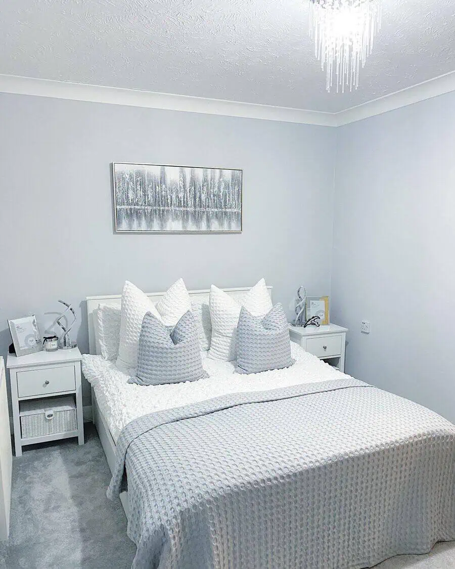 Modern grey and white bedroom with textured bedding, soft lighting, and a serene wall painting.