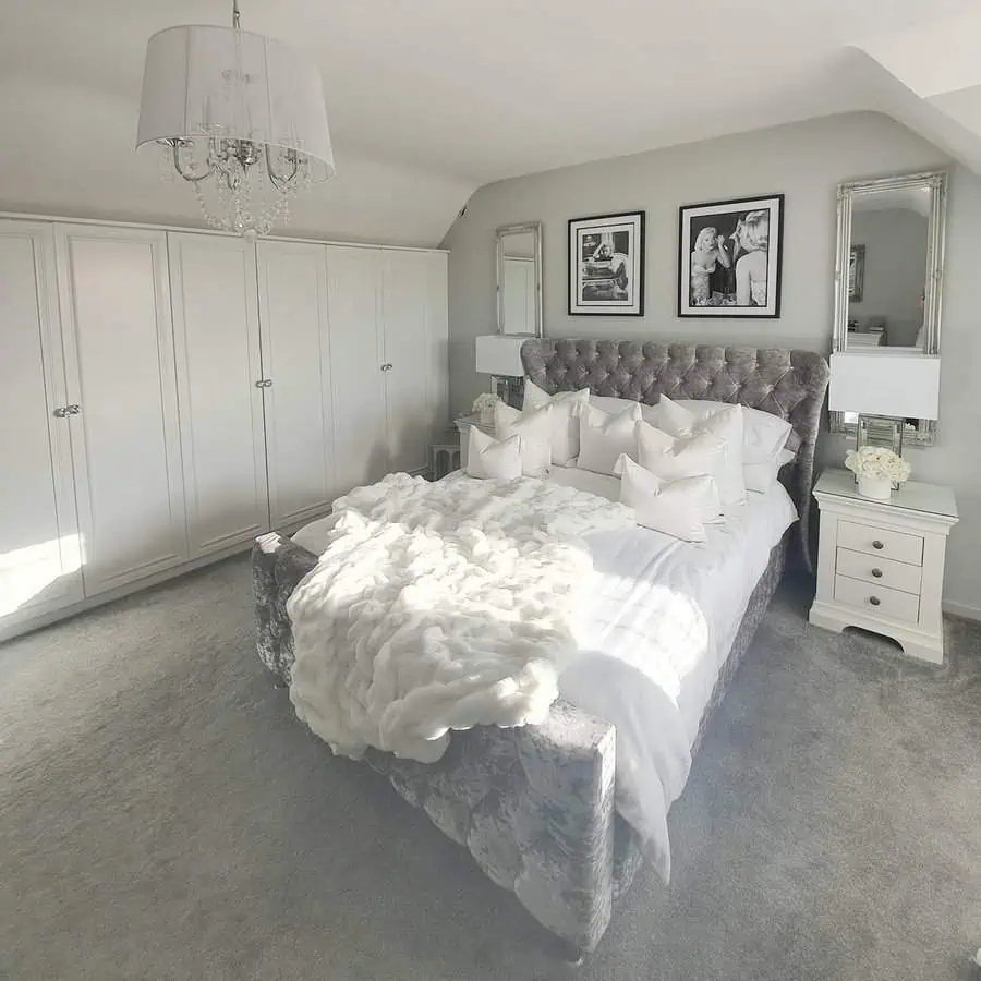 Elegant grey and white bedroom with a tufted bed, plush bedding, and a crystal chandelier.