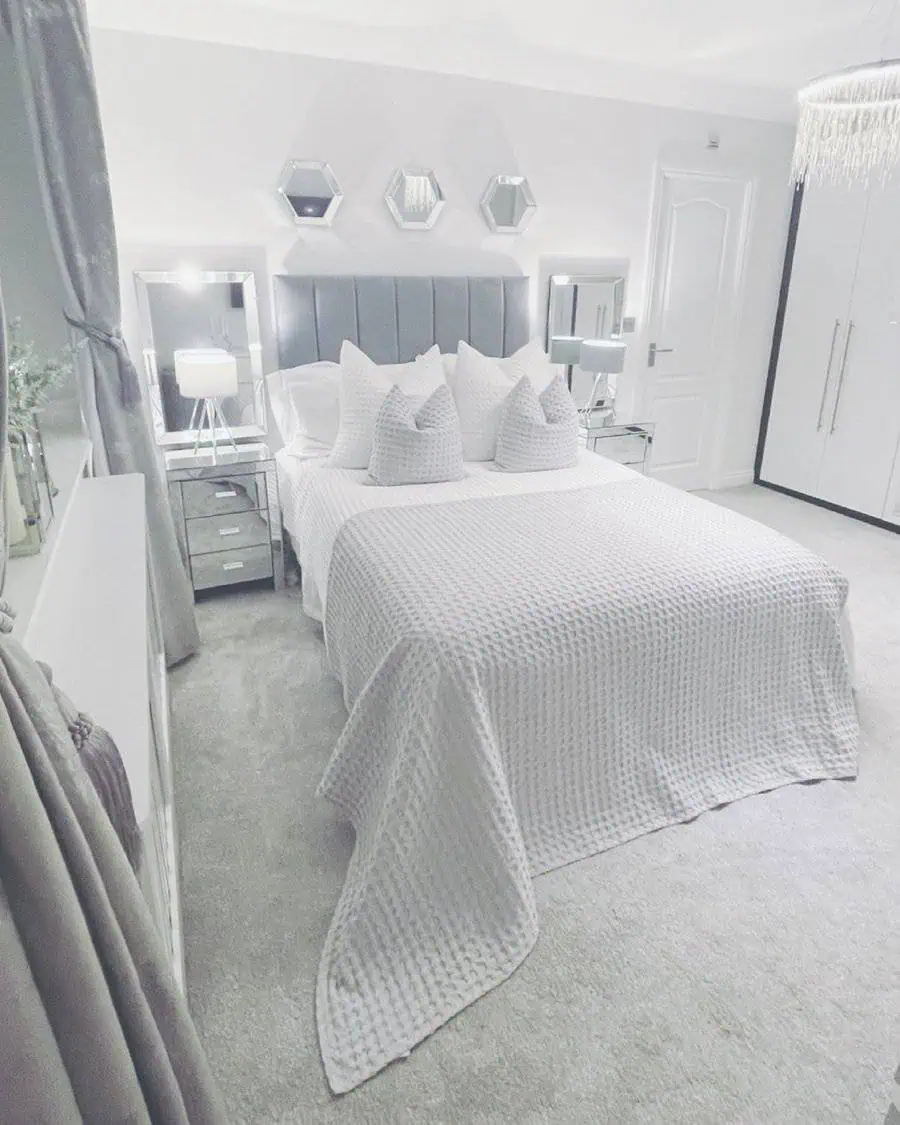 Modern grey and white bedroom with soft lighting, tufted headboard, and elegant mirrored decor.