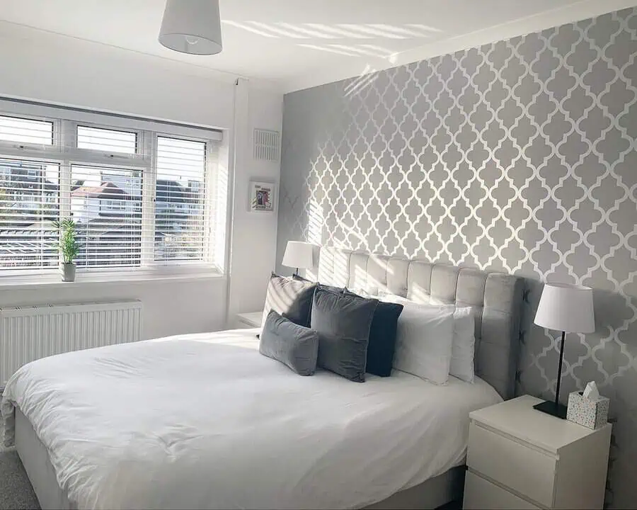 Modern grey and white bedroom with a tufted headboard, patterned accent wall, and soft lighting.