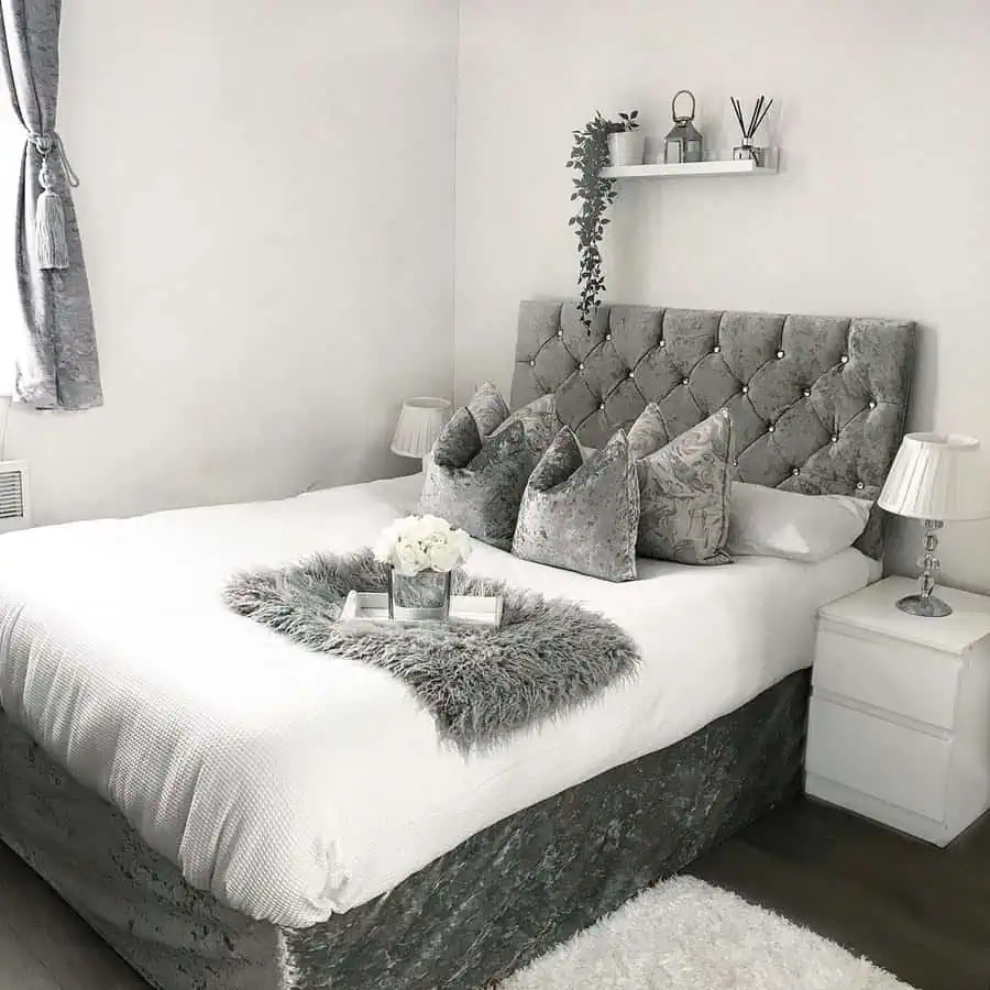 Luxurious grey and white bedroom with a tufted velvet headboard, plush pillows, and soft decor.