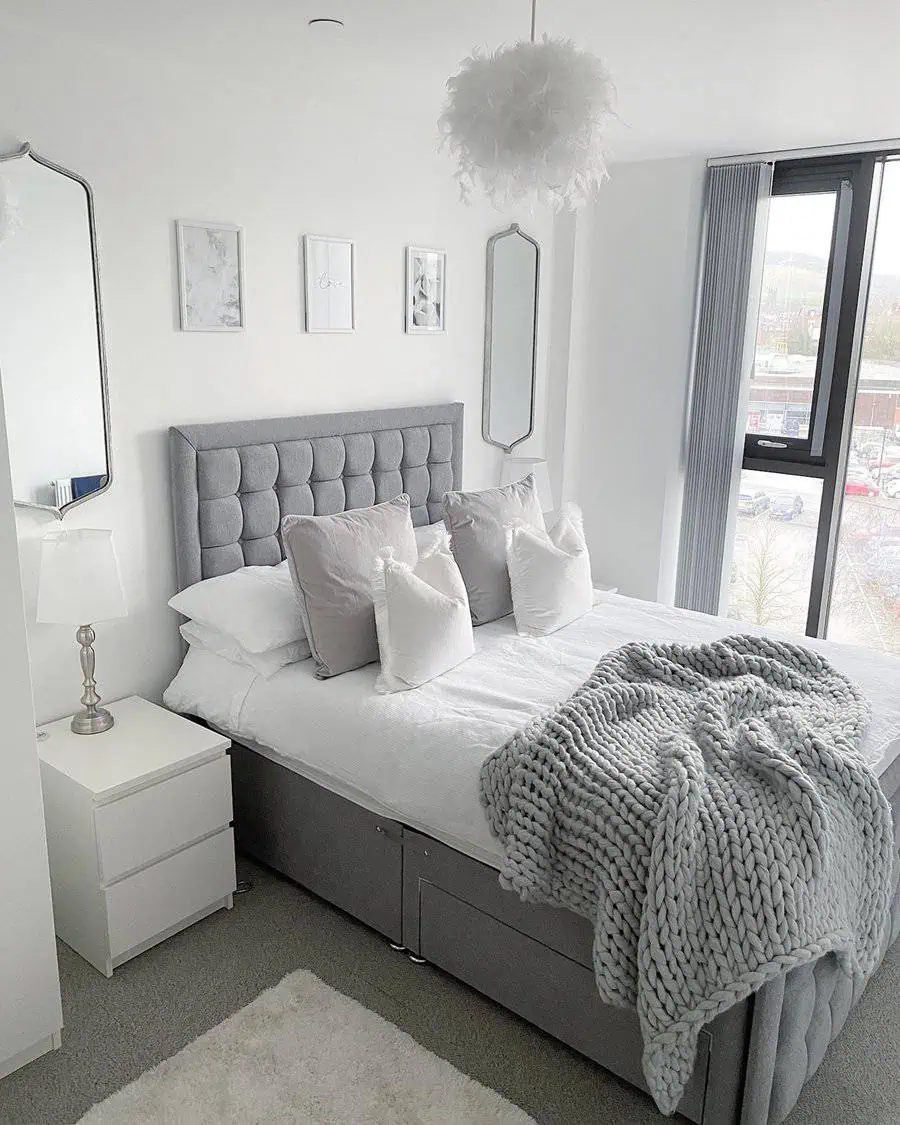 Modern grey and white bedroom with a tufted headboard, fluffy decor, and cozy knit blanket.