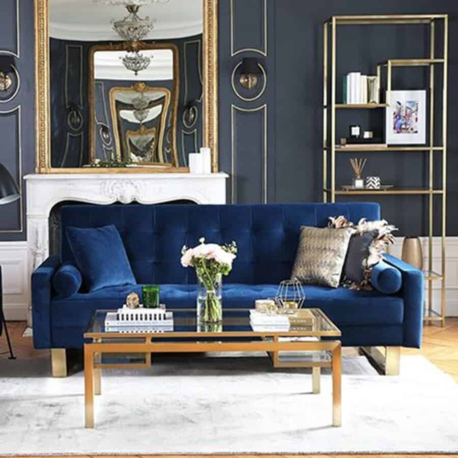 Navy blue living room with a velvet sofa, gold coffee table, and elegant mirror above a fireplace.