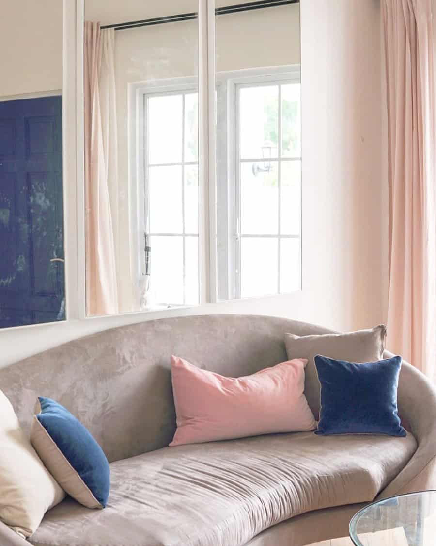 Elegant living room with a curved beige sofa, navy and blush pillows, and large mirrored wall decor.