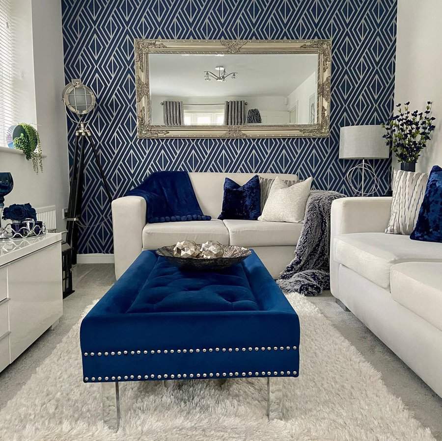 Navy blue and white living room with a geometric accent wall, tufted ottoman, and elegant decor.
