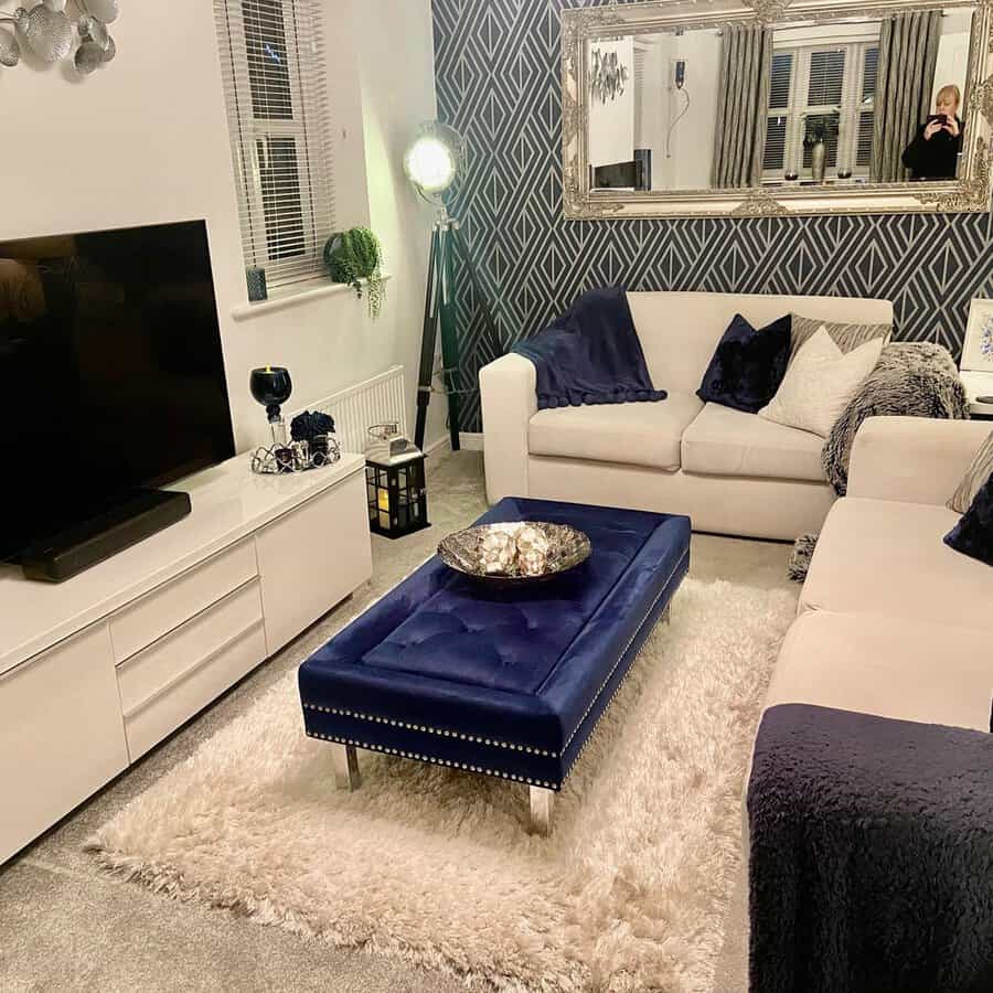 Navy blue and cream living room with a tufted ottoman, geometric accent wall, and plush textures.