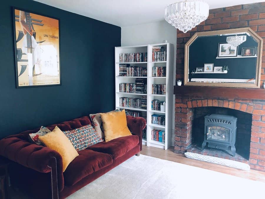 Navy blue living room with a burgundy velvet sofa, brick fireplace, and gold-accented decor.
