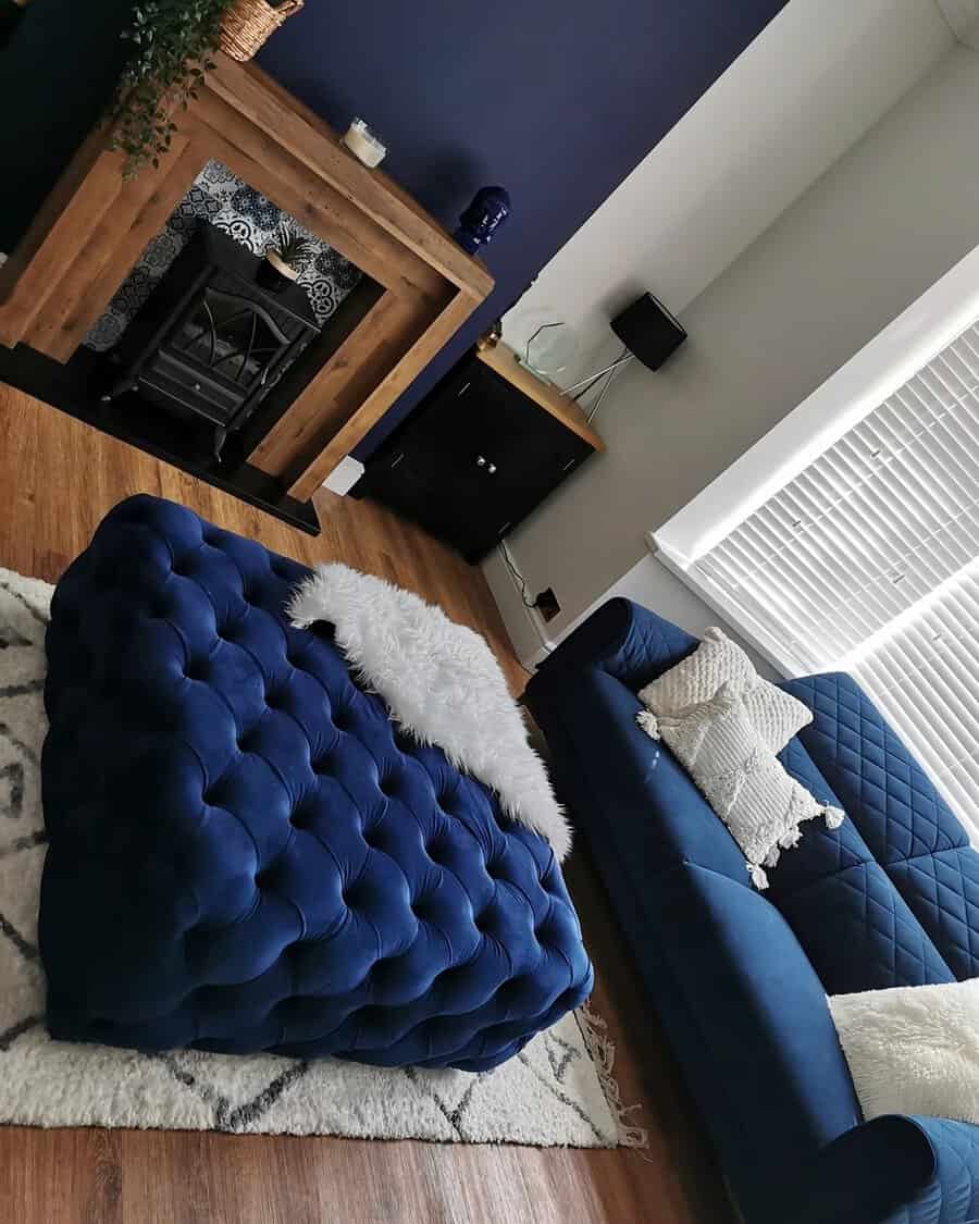 Navy blue living room with a bold accent wall, tufted ottoman, cozy sofa, and wooden fireplace mantel.