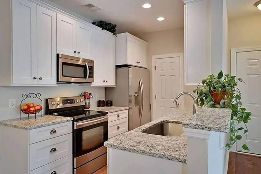 Compact galley-style open kitchen with white cabinets, granite countertops, and stainless steel appliances.