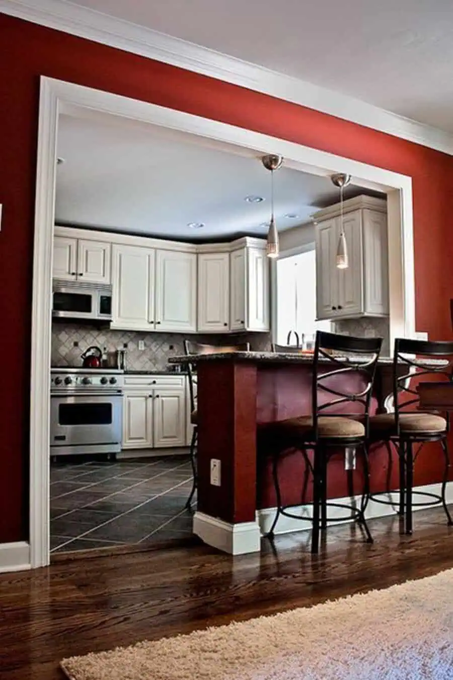 Open kitchen with bold red accent walls, white cabinetry, and a raised bar seating area.