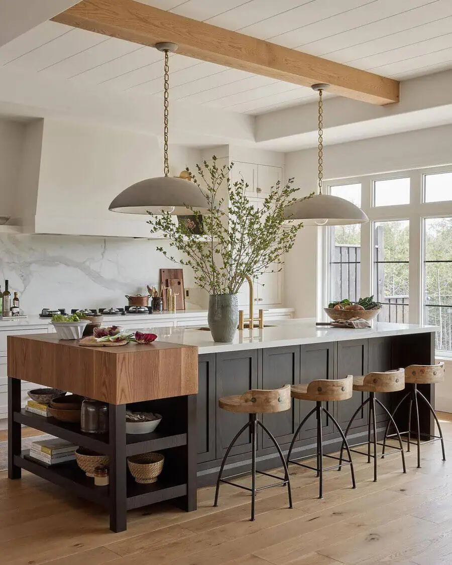 Modern farmhouse kitchen with a dark island, wood accents, large windows, and statement lighting.