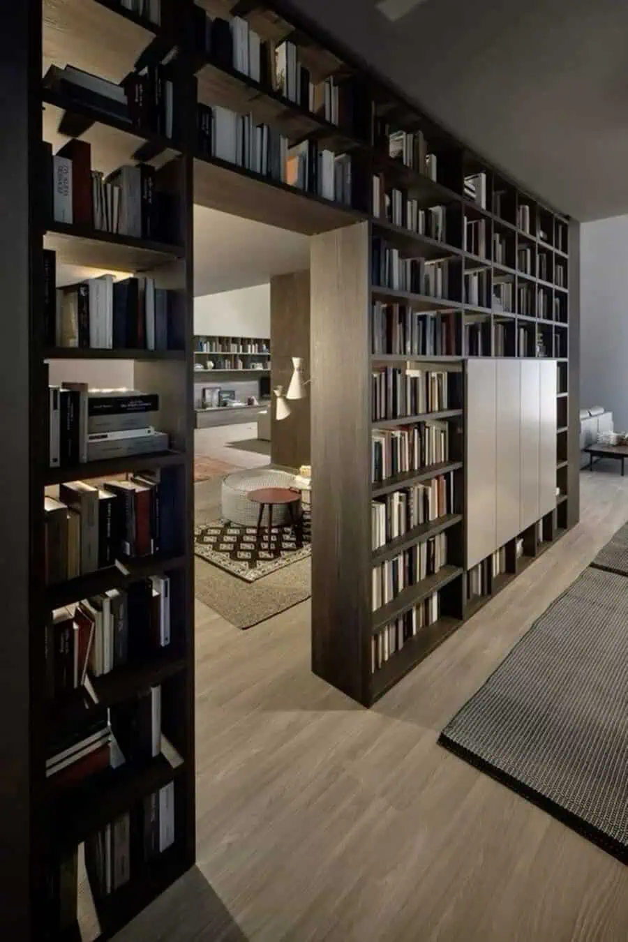 Open-plan home library with floor-to-ceiling dark wood bookshelves, hidden doorway, and cozy seating.