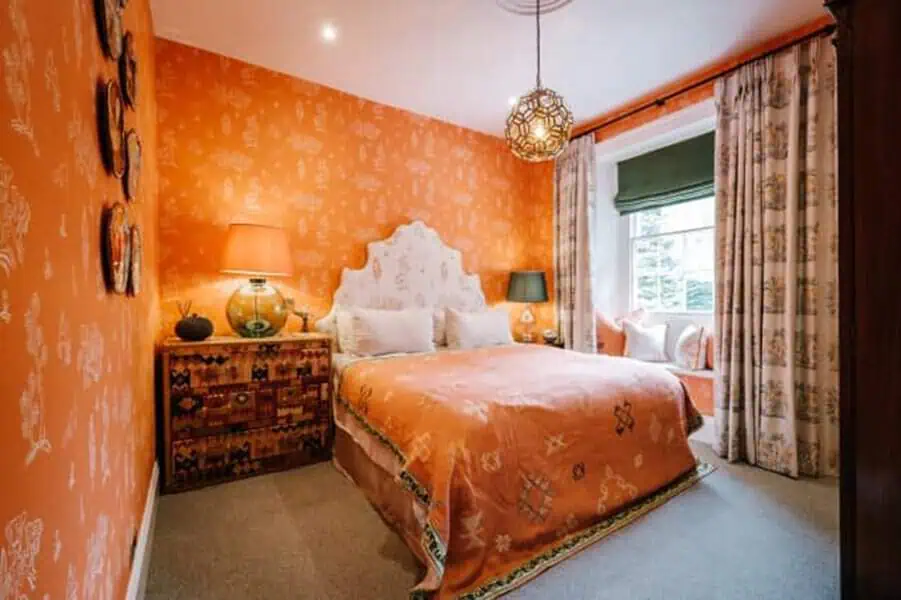 Orange bedroom with an artistic wall mural, intricate patterns, warm lighting, and cozy furnishings.