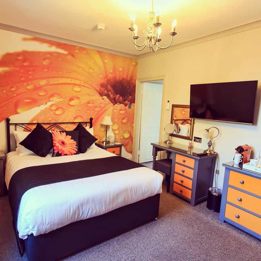 Orange bedroom with a bold floral wall mural, black and orange furniture, and a cozy modern design.