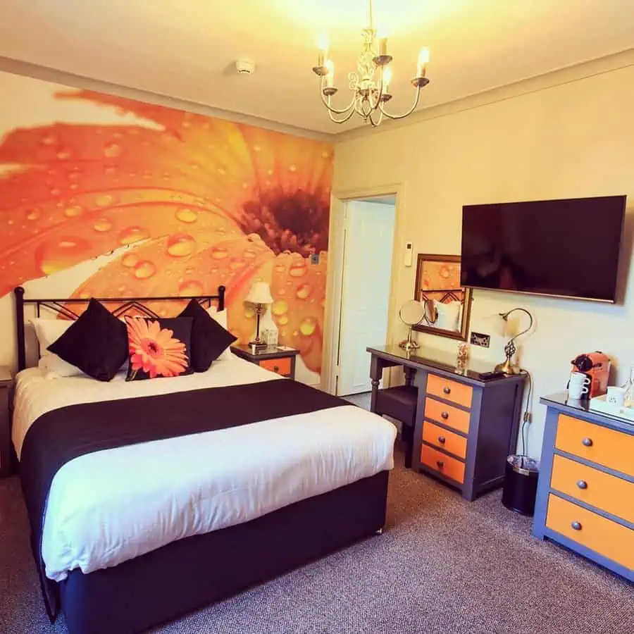 Orange bedroom with a bold floral wall mural, black and orange furniture, and a cozy modern design.