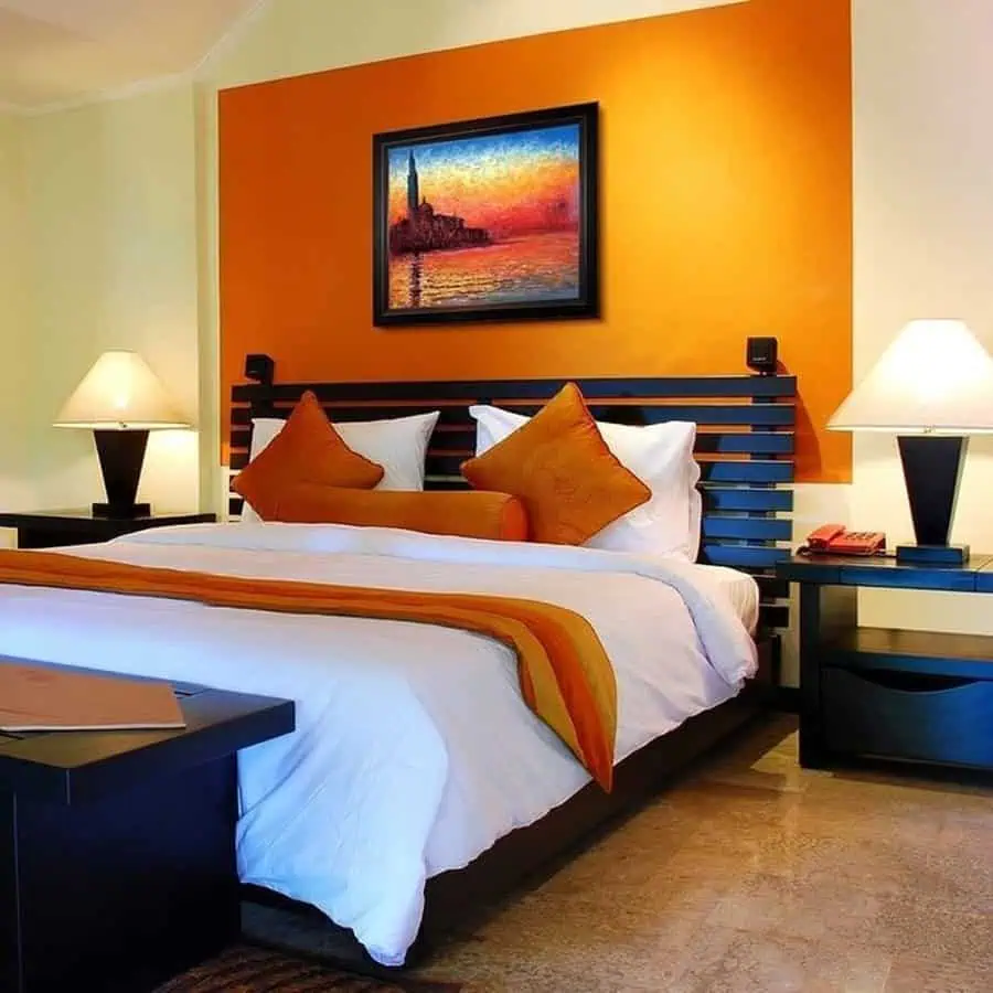 Orange bedroom with warm lighting, cozy bedding, dark wood furniture, and a stylish accent wall.