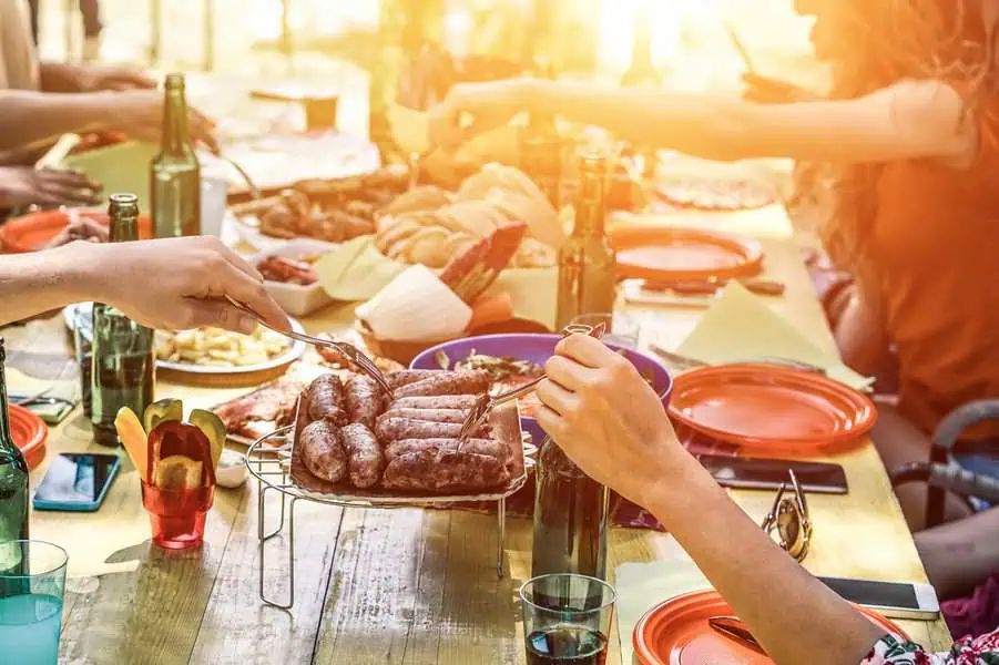 Outdoor housewarming barbecue party with grilled sausages, fresh bread, and friends enjoying the meal.