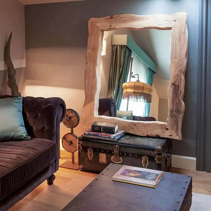 Rustic wooden-framed mirror reflecting a cozy living room with vintage furniture and warm lighting.