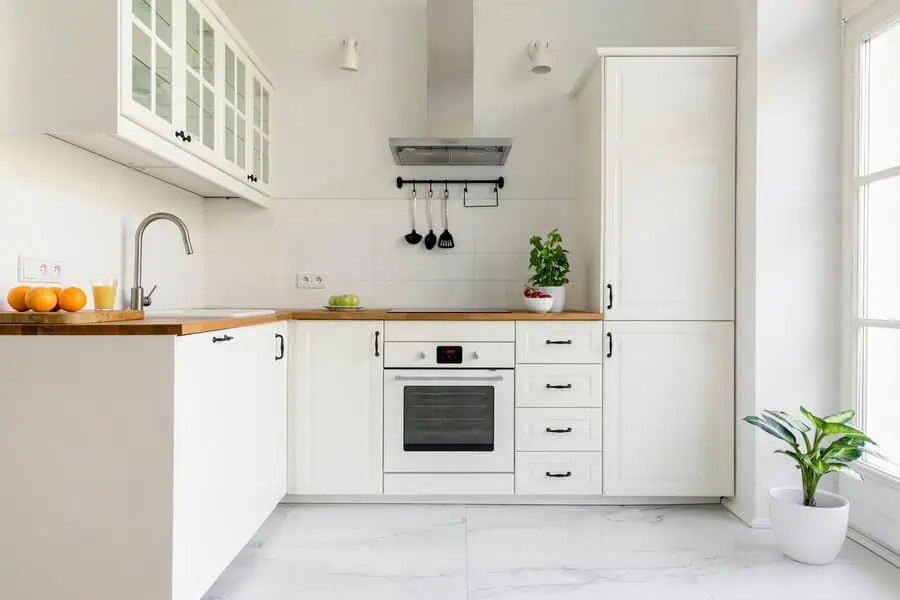 Simple kitchen with white cabinetry, wooden countertops, and greenery for a fresh and airy feel.