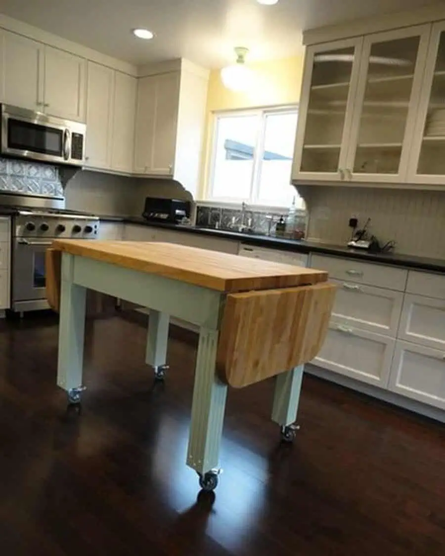 Simple kitchen design with white cabinets, dark countertops, and a rolling butcher block island.