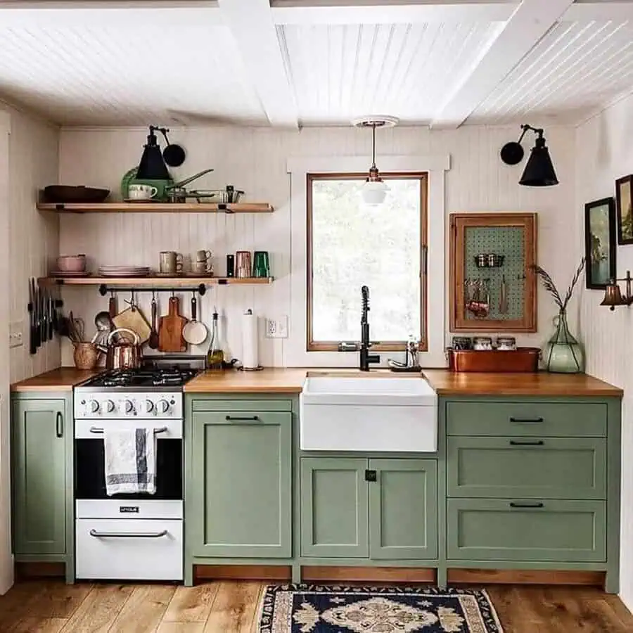 Simple kitchen design with sage green cabinets, wooden countertops, open shelving, and a farmhouse sink.