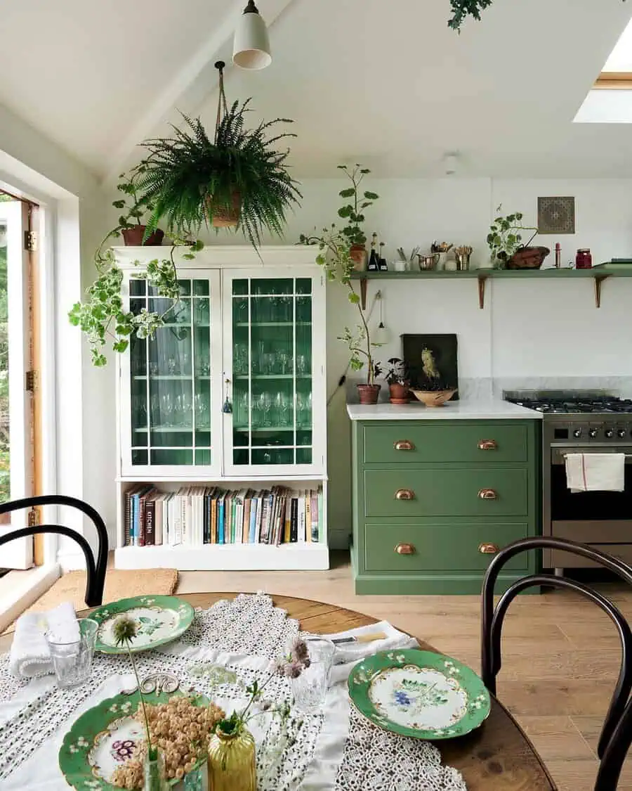 Simple kitchen with green cabinetry, open shelving, and lush greenery for a fresh, natural look.