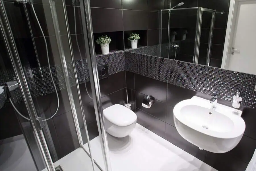 Small black bathroom with mosaic tile accents, glass shower, and modern white fixtures.