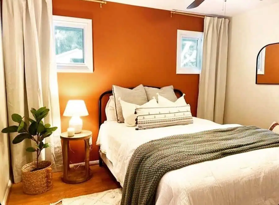 Small bedroom with an orange accent wall, white bedding, neutral decor, and a knit throw.