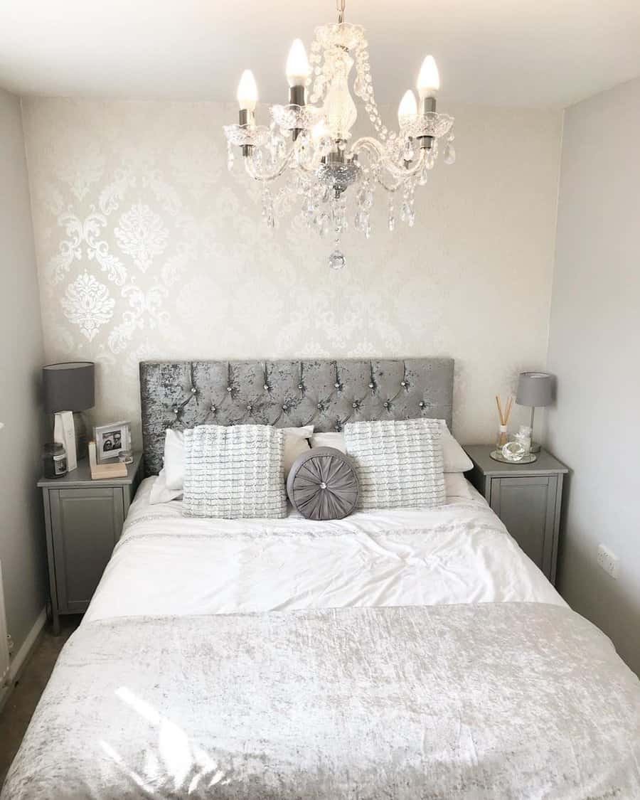 Elegant grey and white bedroom with a tufted headboard, crystal chandelier, and soft bedding.