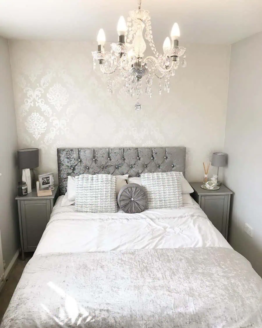 Elegant grey and white bedroom with a tufted headboard, crystal chandelier, and soft bedding.