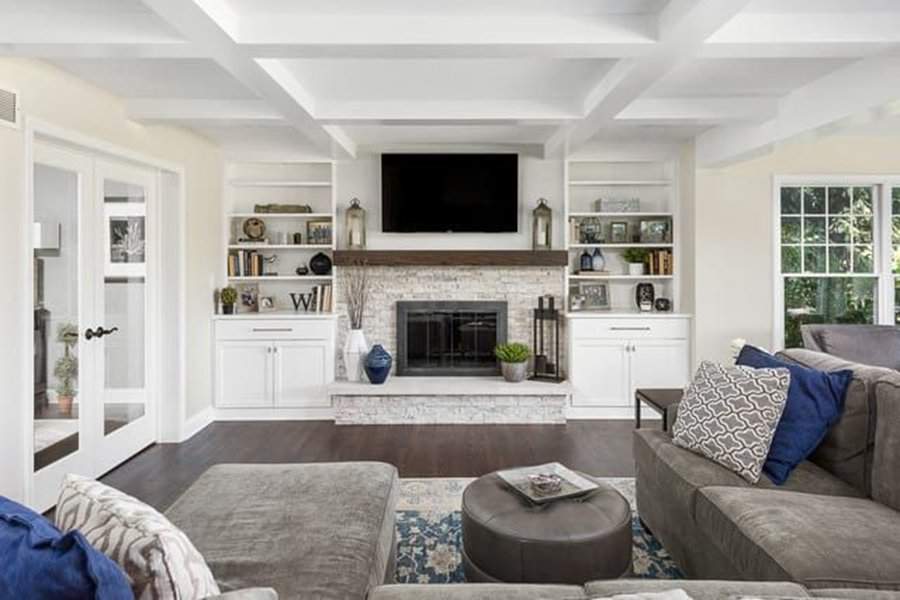 Sophisticated living room with a coffered ceiling, stone fireplace, built-in shelves, and gray sofa.