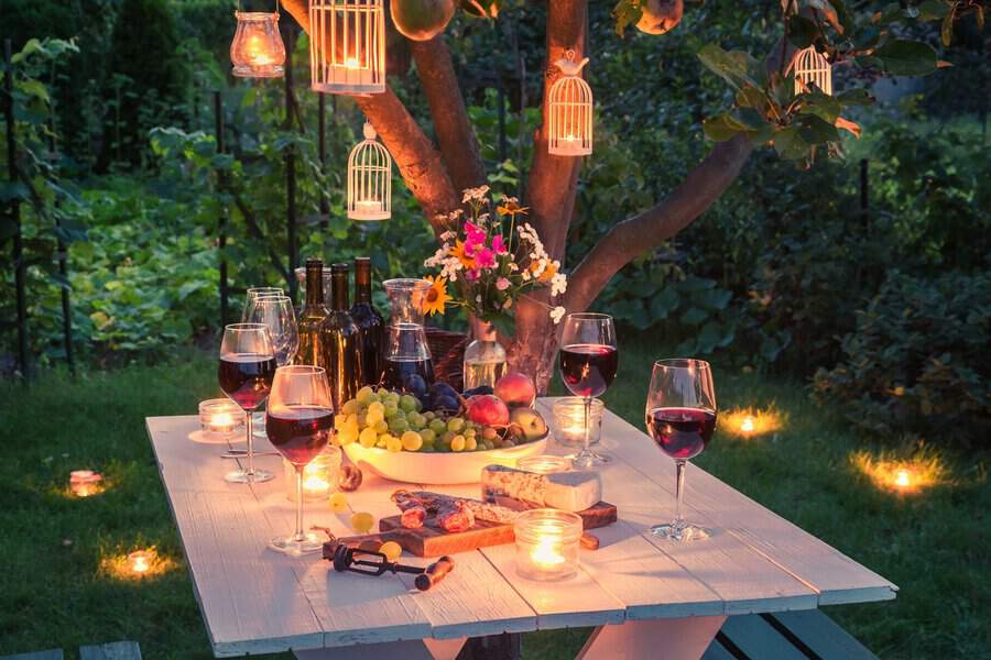 Spring garden housewarming party with a candlelit table, wine, fresh fruit, and a charming outdoor setting.