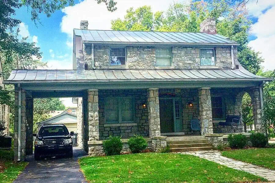 Stone Dutch Colonial house with a metal roof, arched porch, and an attached carport garage.