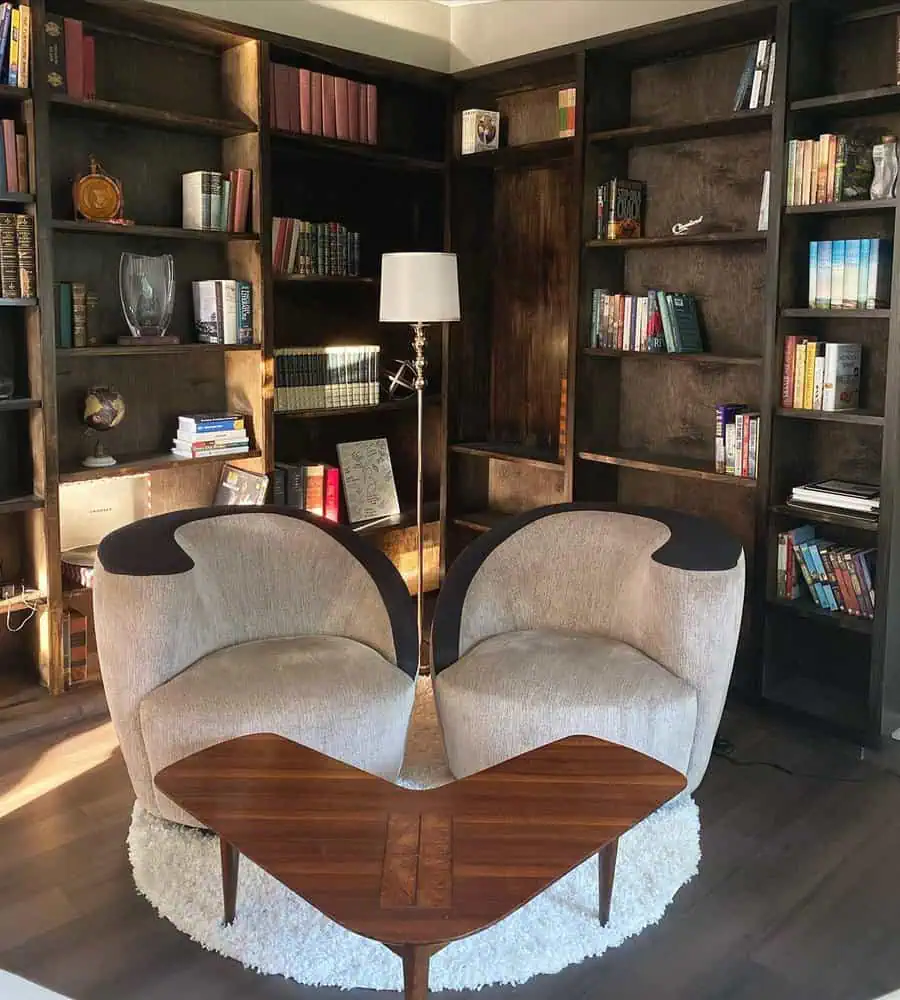 Stylish home library with dark wood bookshelves, modern seating, and warm lighting.