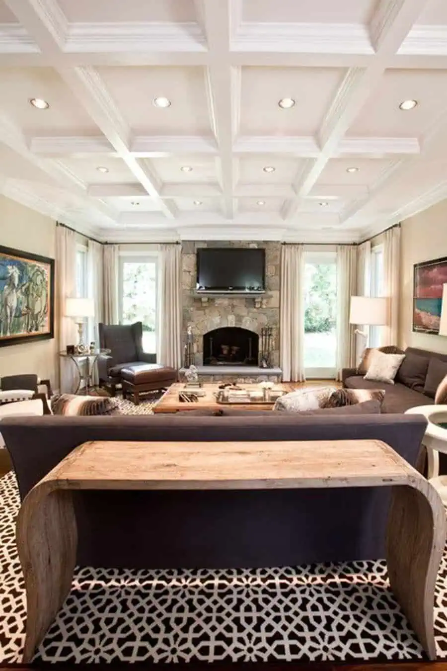 Traditional living room with a modern coffered ceiling, stone fireplace, elegant seating, and warm decor.