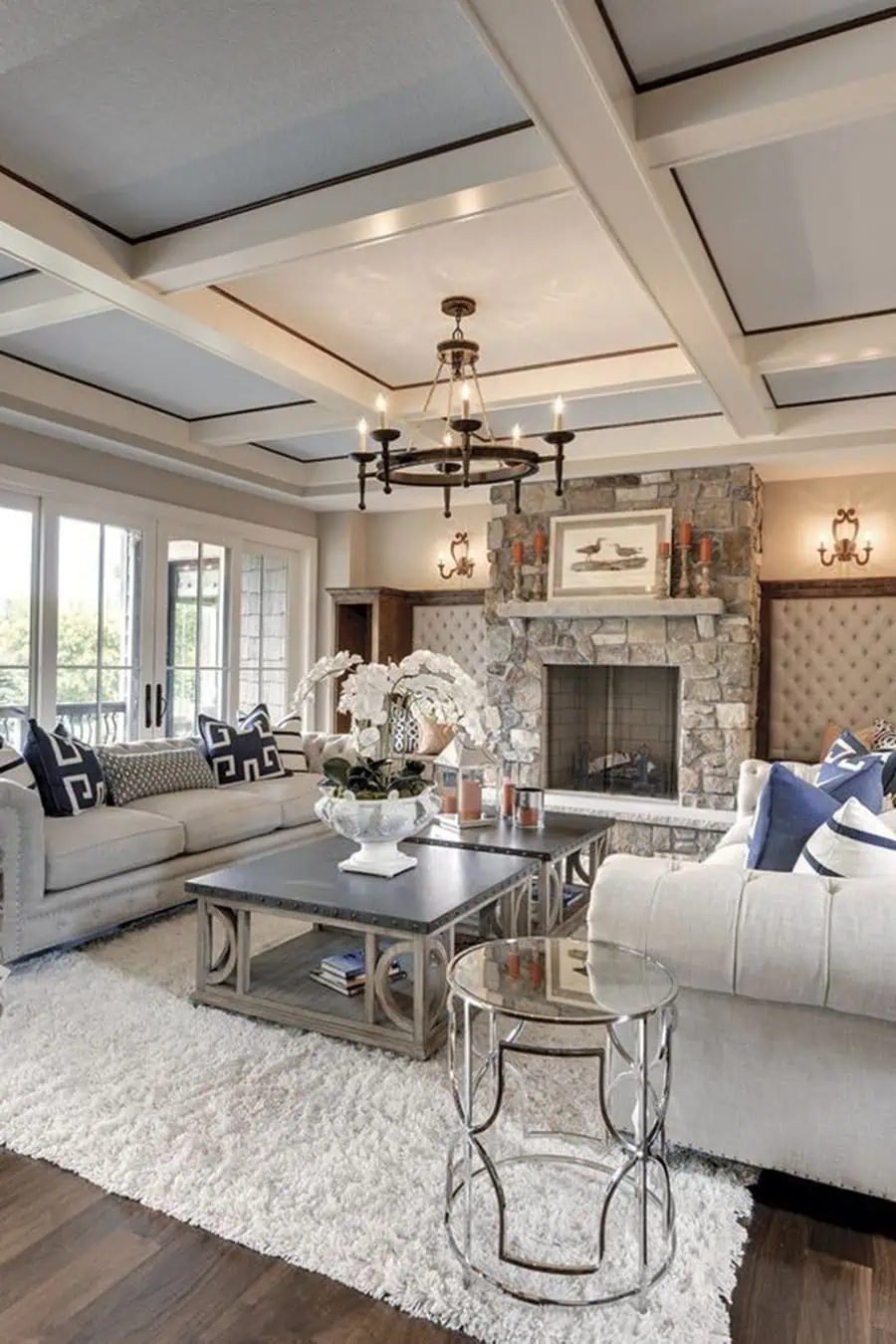 Traditional living room with a modern coffered ceiling, stone fireplace, tufted seating, and elegant decor.