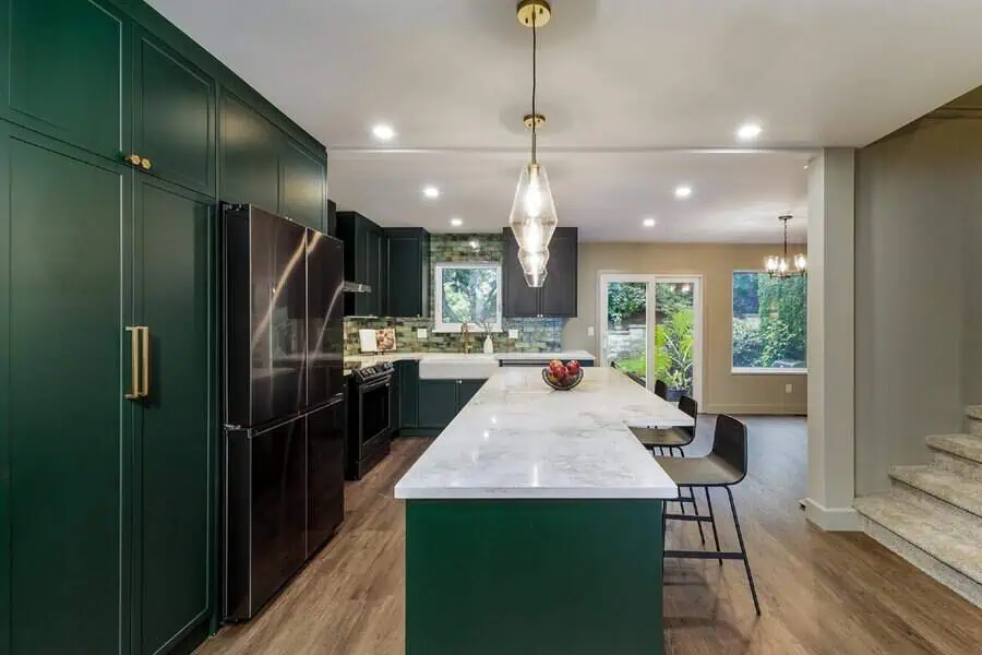 Transitional open kitchen with deep green cabinets, marble island, and elegant pendant lighting.