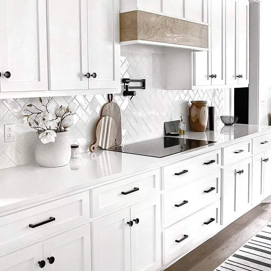 White herringbone backsplash and white countertop create a seamless, bright, and elegant look with white cabinets.