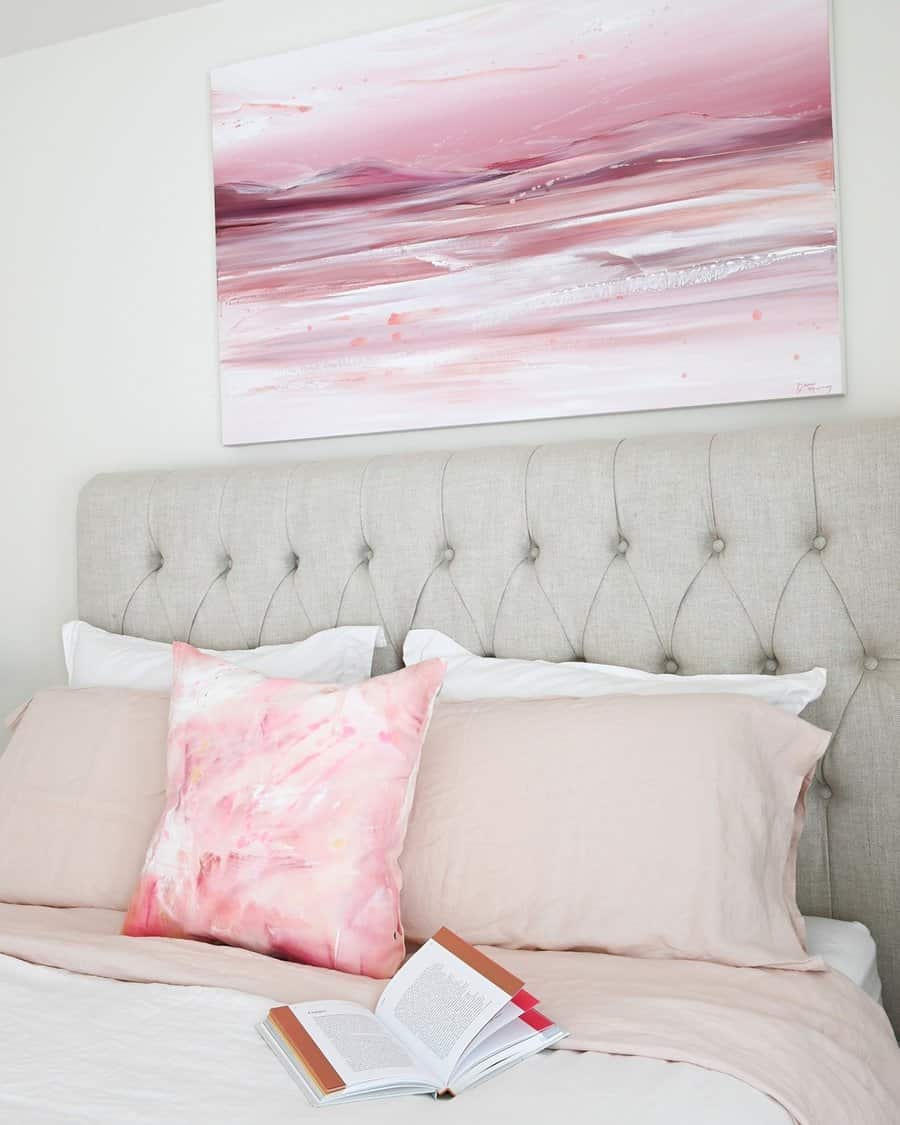 Abstract pink artwork above a tufted headboard adds movement and depth to a serene, modern bedroom.
