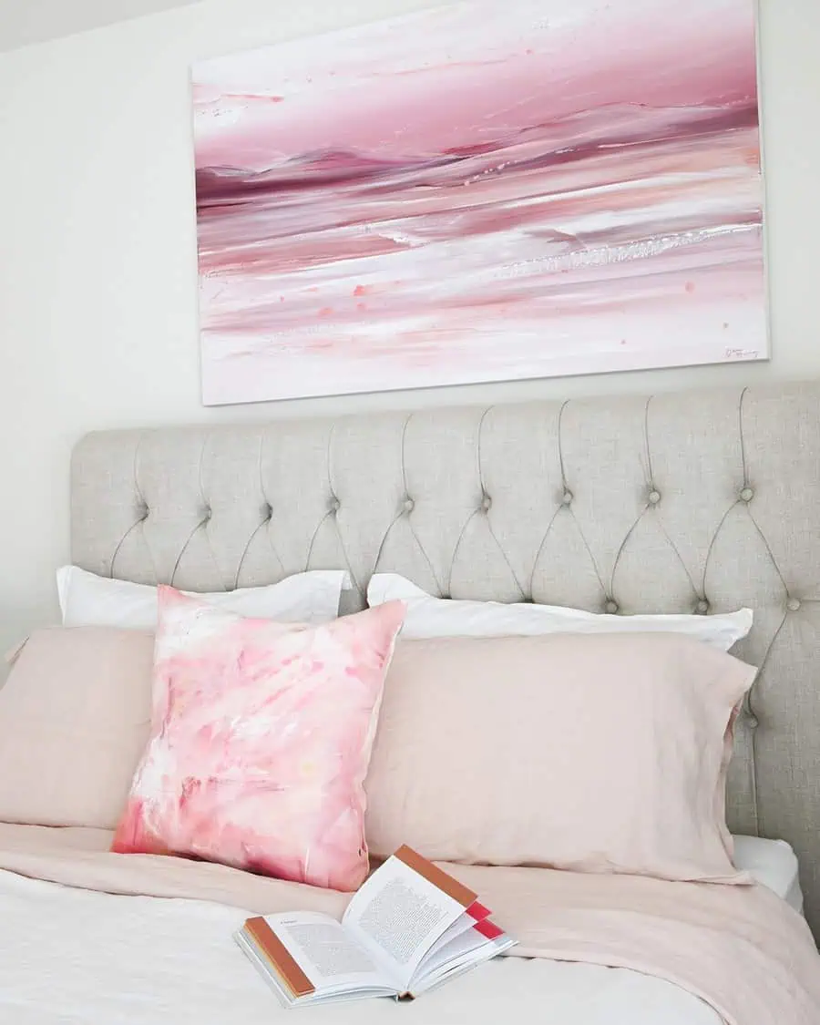 Abstract pink artwork above a tufted headboard adds movement and depth to a serene, modern bedroom.