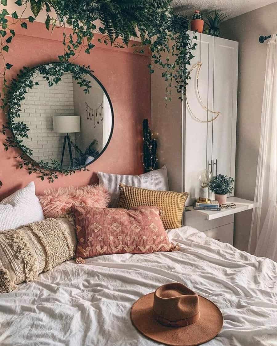 Warm pink accent wall with a round mirror, cascading greenery, and boho-inspired decor for a cozy and inviting bedroom.