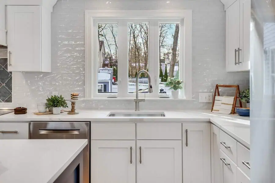 Modern white kitchen with triple casement window above sink, letting in natural light. White counters and cabinetry.