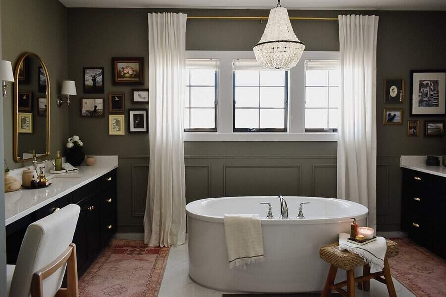 Beaded empire chandelier above a white soaking tub in a green-walled bathroom with drapery and curated artwork.