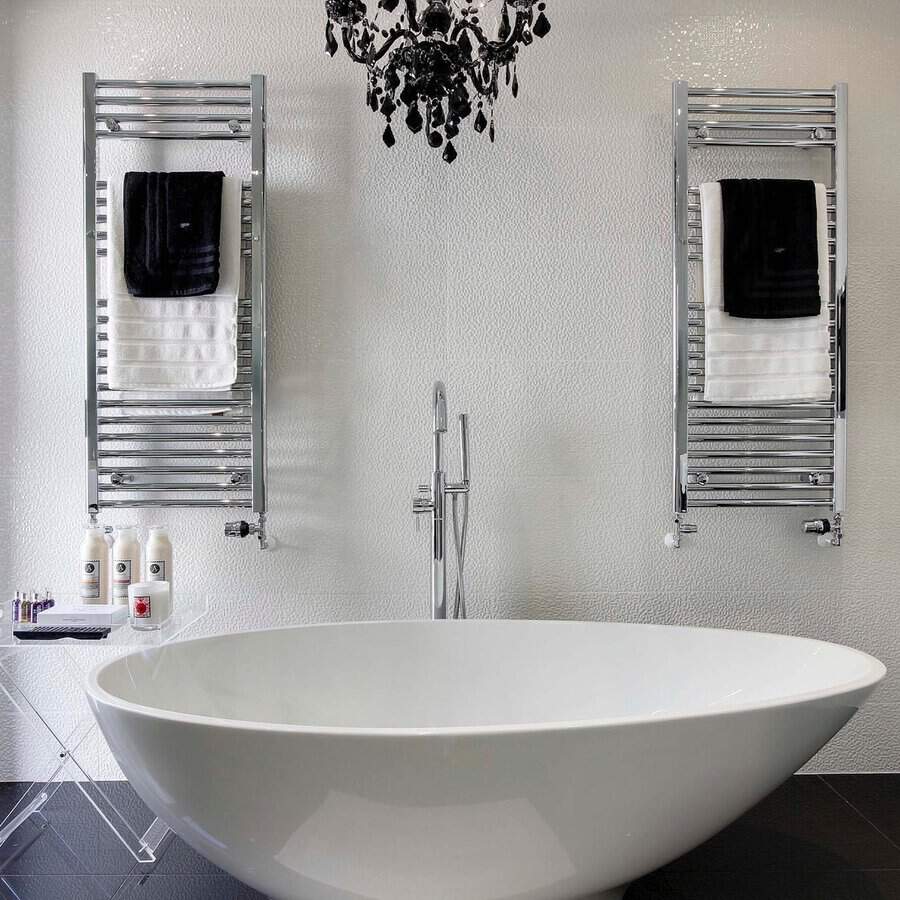 Black chandelier above a white freestanding tub, chrome towel warmers, and textured walls in a modern black-and-white bathroom.