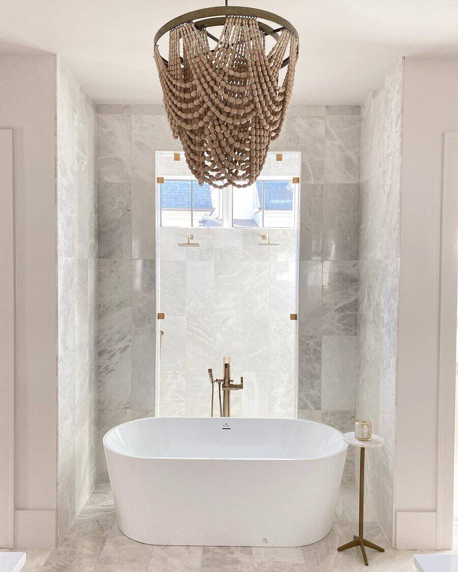 Wood-bead chandelier above a white freestanding tub framed by marble walls and brass accents.