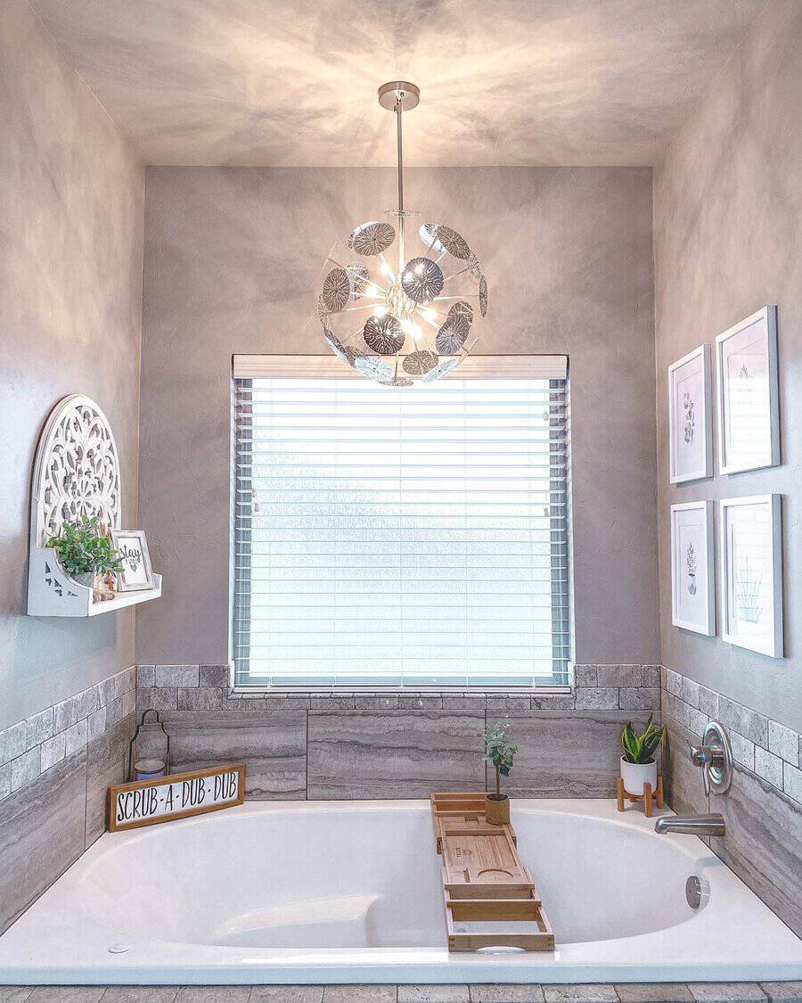 Metal leaf globe light above a built-in tub, gray walls, wooden bath caddy, and subtle decorative accents.