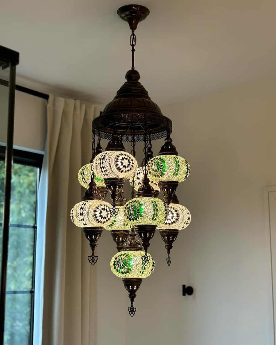 Mosaic lanterns suspended above a white soaking tub, framed by neutral curtains and a dark-framed window.