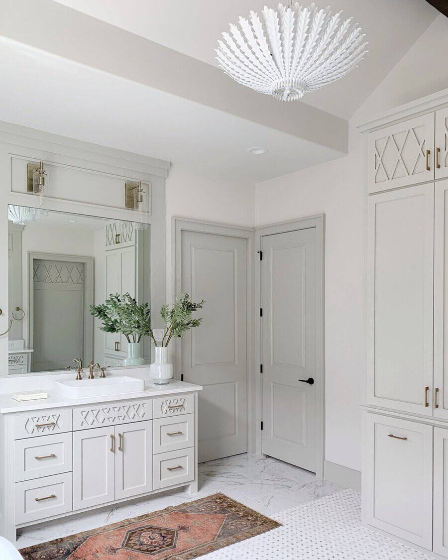 White sculptural chandelier in a neutral bathroom with decorative cabinets, brass fixtures, and a vintage-inspired rug.