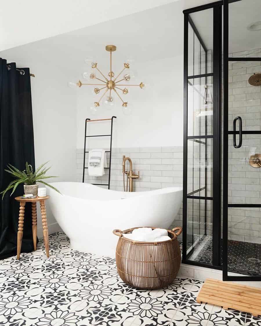 Sputnik-style chandelier above a white freestanding tub, black-framed shower, and bold patterned floor tile.